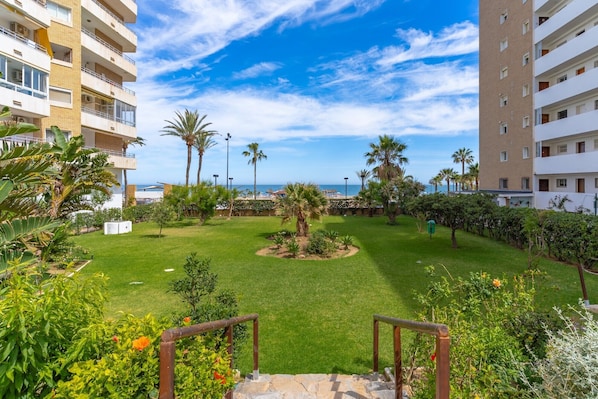 A courtyard with a lawn, palm trees, and a view of the sea. - Holiday Apartment "Fuengirola" with Sea and Mountain View, Shared Pool & Wi-Fi (Fuengirola)