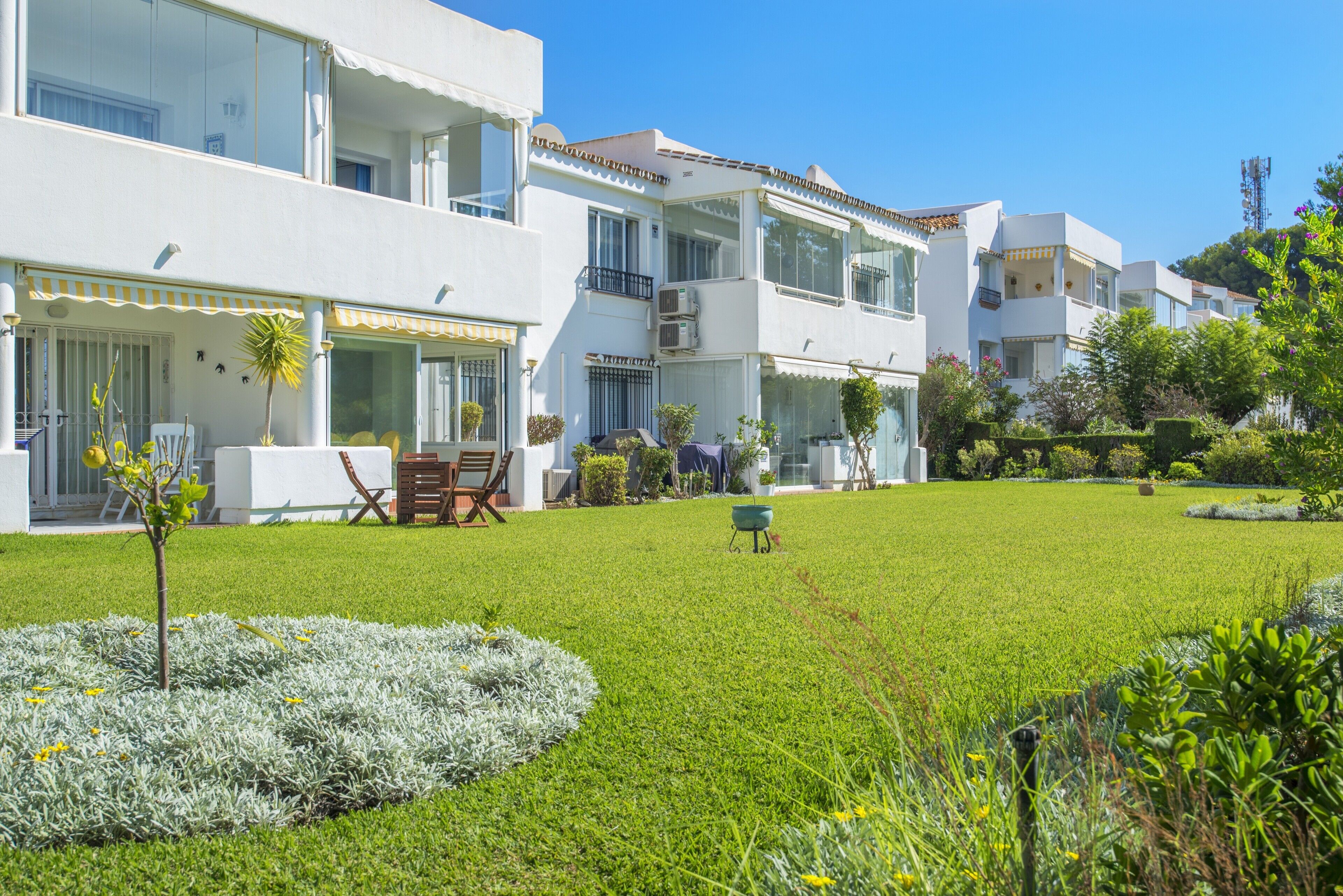 Un immeuble résidentiel moderne à plusieurs étages, doté de balcons, d’une pelouse bien entretenue et de mobilier d’extérieur.