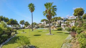 Un giardino curato con palme, una piscina e un cielo sereno.