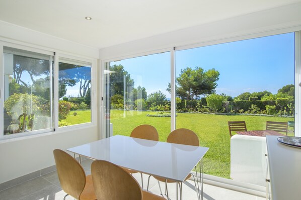 Un comedor con mesa y sillas, ventanas amplias y vista a un jardín cuidado.