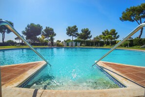 Una piscina con agua cristalina azul, rodeada de árboles y un césped cuidado.