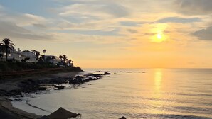 Una spiaggia con ombrelloni di paglia, mare calmo e tramonto.