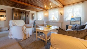Una sala de estar acogedora con techo de madera, un sofá blanco, un sofá beige, una mesa de comedor con un bol y un cuadro en la pared.