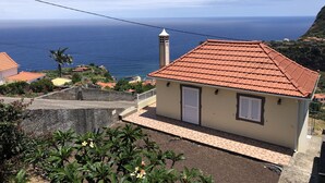 Uma casa à beira-mar com telhado de telhas vermelhas, uma pequena varanda e vista para o mar.