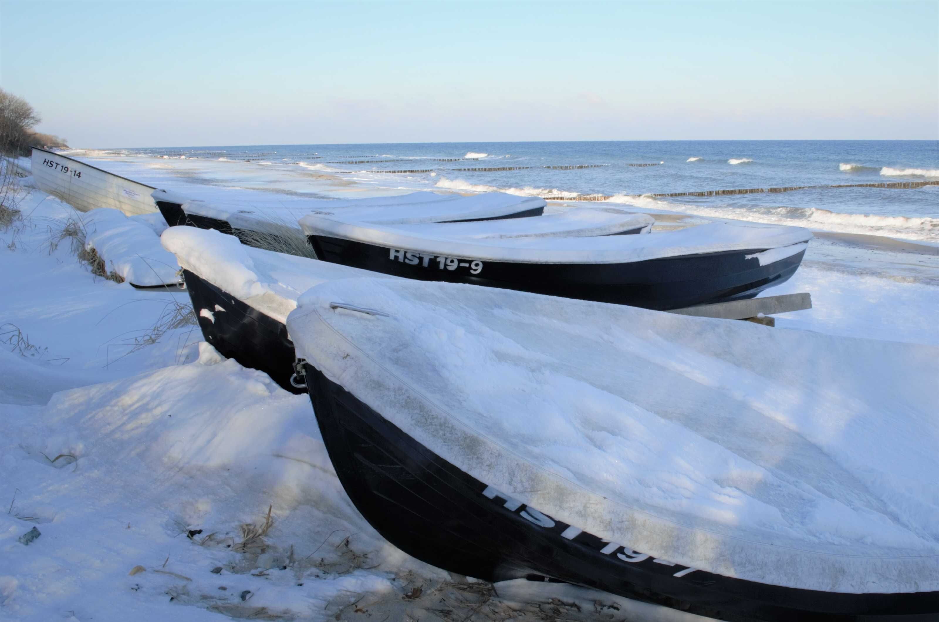 A row of boats covered in snow on a beach.