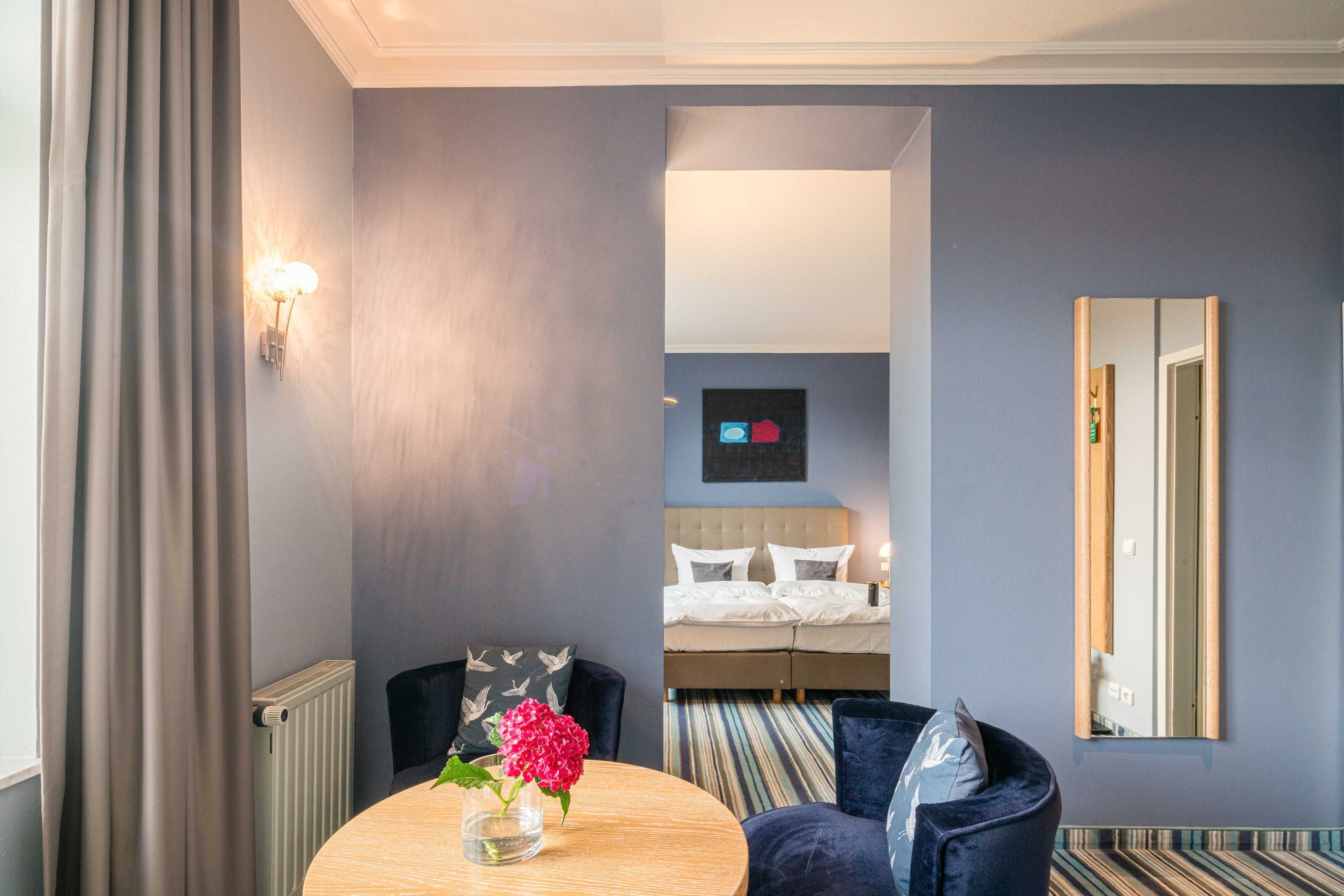 Ein Hotelzimmer mit rundem Tisch, einem Sessel, einem Bett mit Kopfteil, einem Spiegel und einer Heizung.