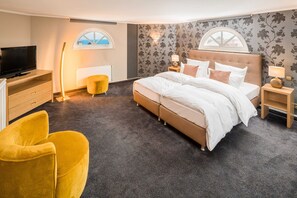 A bedroom with a bed, a TV, a yellow chair, and a window. - DZ - Hotel Residenz Waldkrone Kühlungsborn (Kühlungsborn)