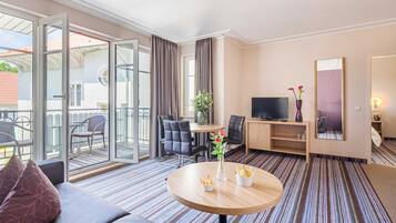 A hotel room with a sofa, a round table with a vase, a TV, a desk, and a chair.