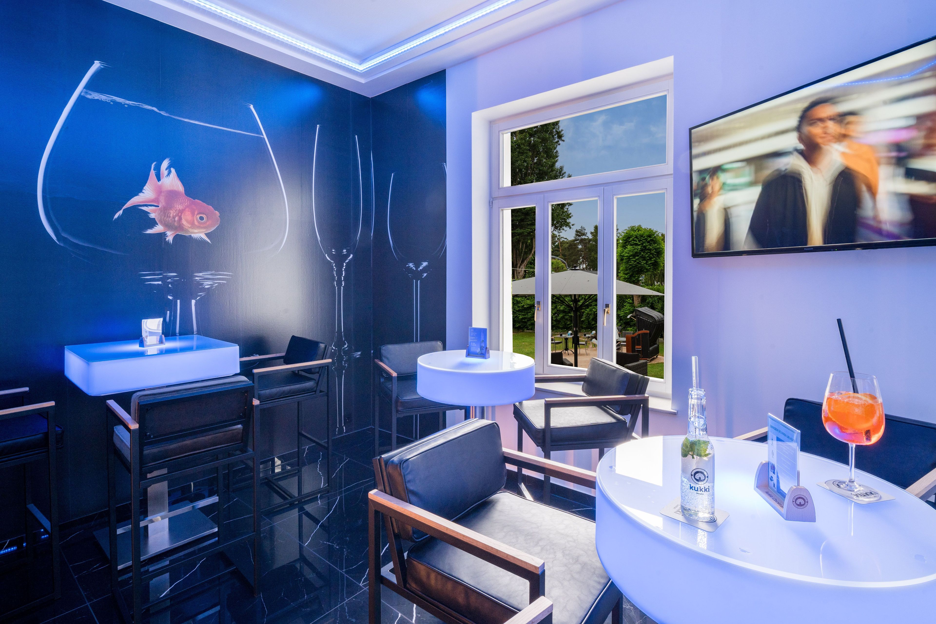 Un espace bar moderne avec un aquarium, des tabourets de bar, un écran de télévision et un cocktail sur la table.