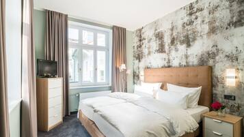 Ein Hotelzimmer mit Bett, Fernseher, Nachttisch, Lampe und einem Fenster mit Vorhängen.