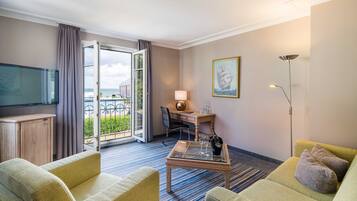 Une chambre d’hôtel équipée d’un canapé, d’une table basse, d’un bureau, d’une télévision, d’une lampe, d’un tableau et offrant une vue à travers une porte vitrée.
