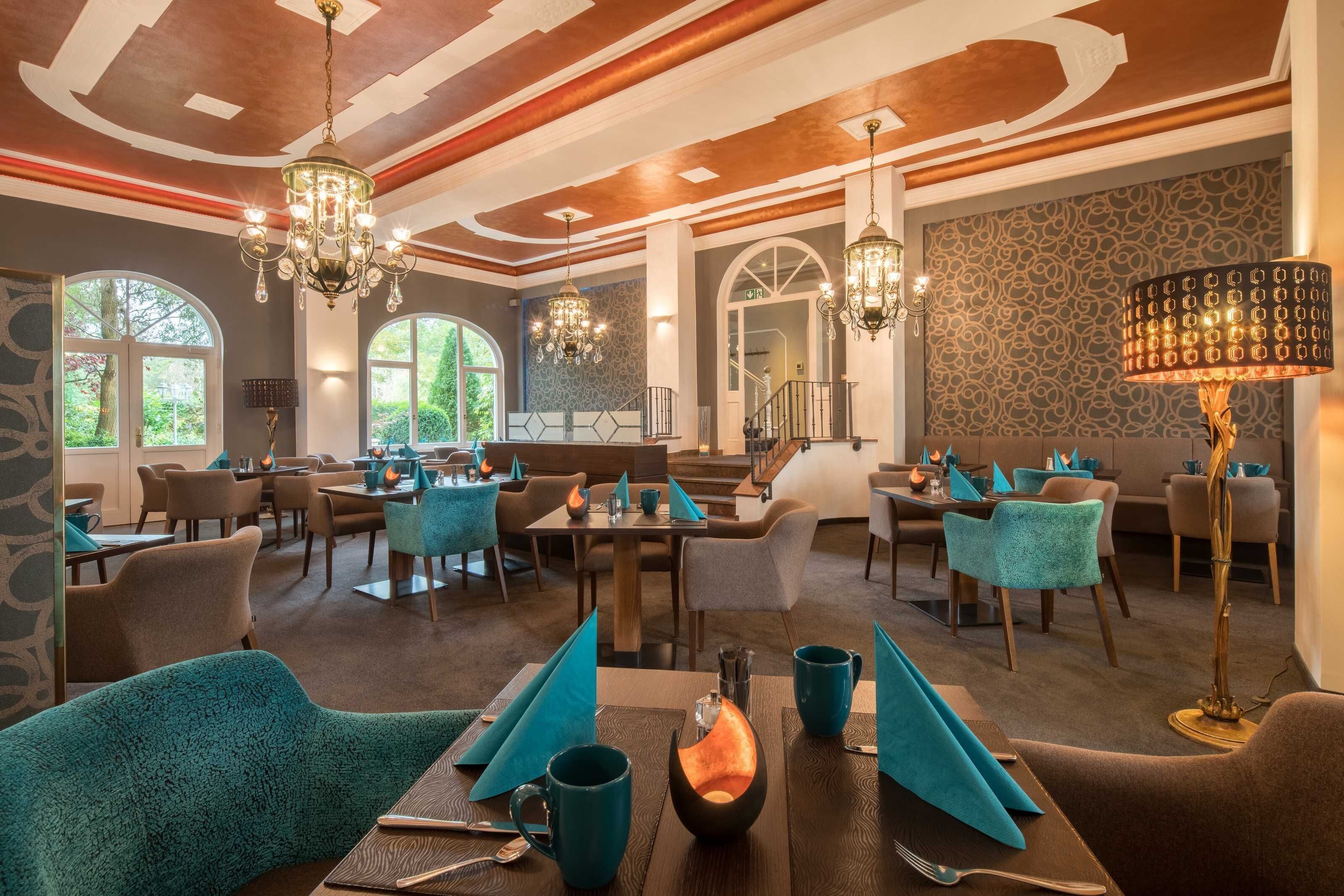 A restaurant with multiple dining tables, chairs, and chandeliers.