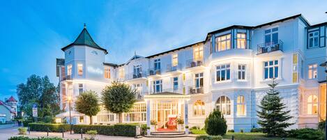 A large, multi-story hotel with a prominent tower, a well-lit entrance, and a landscaped garden.