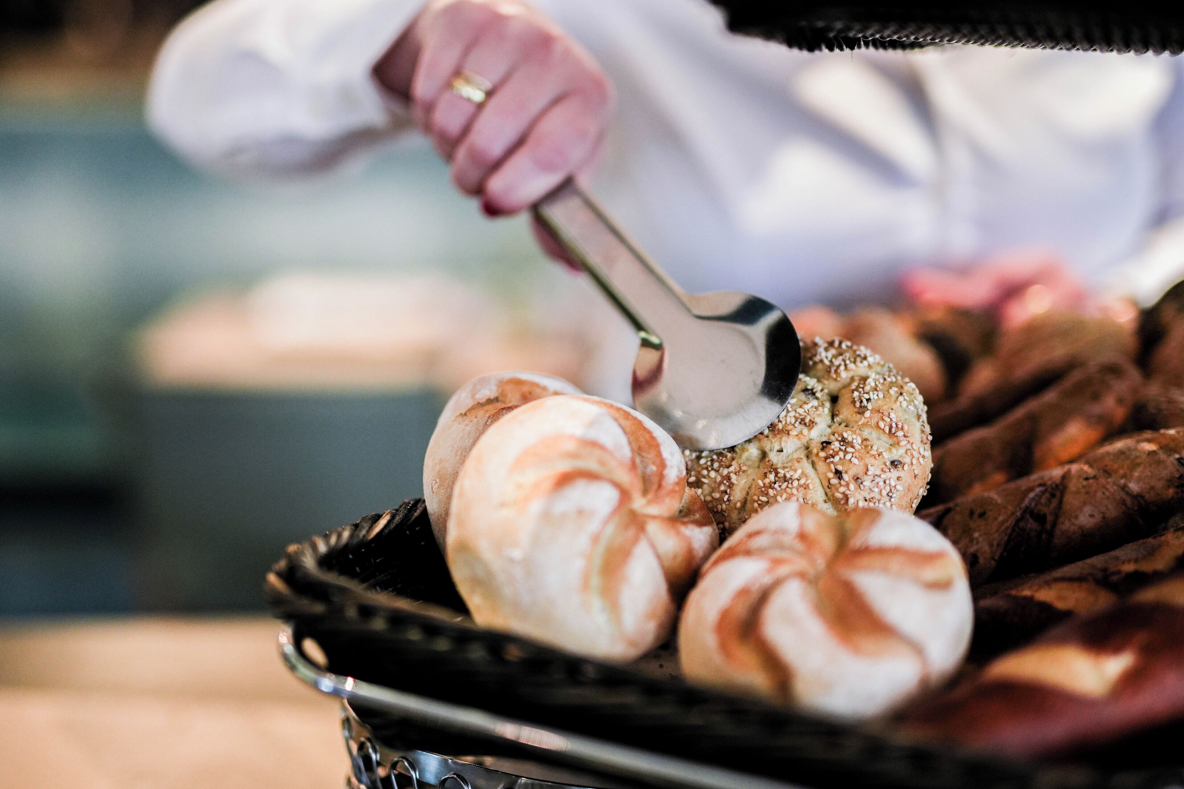 En person använder en tång för att hantera brödrullar på en grill.