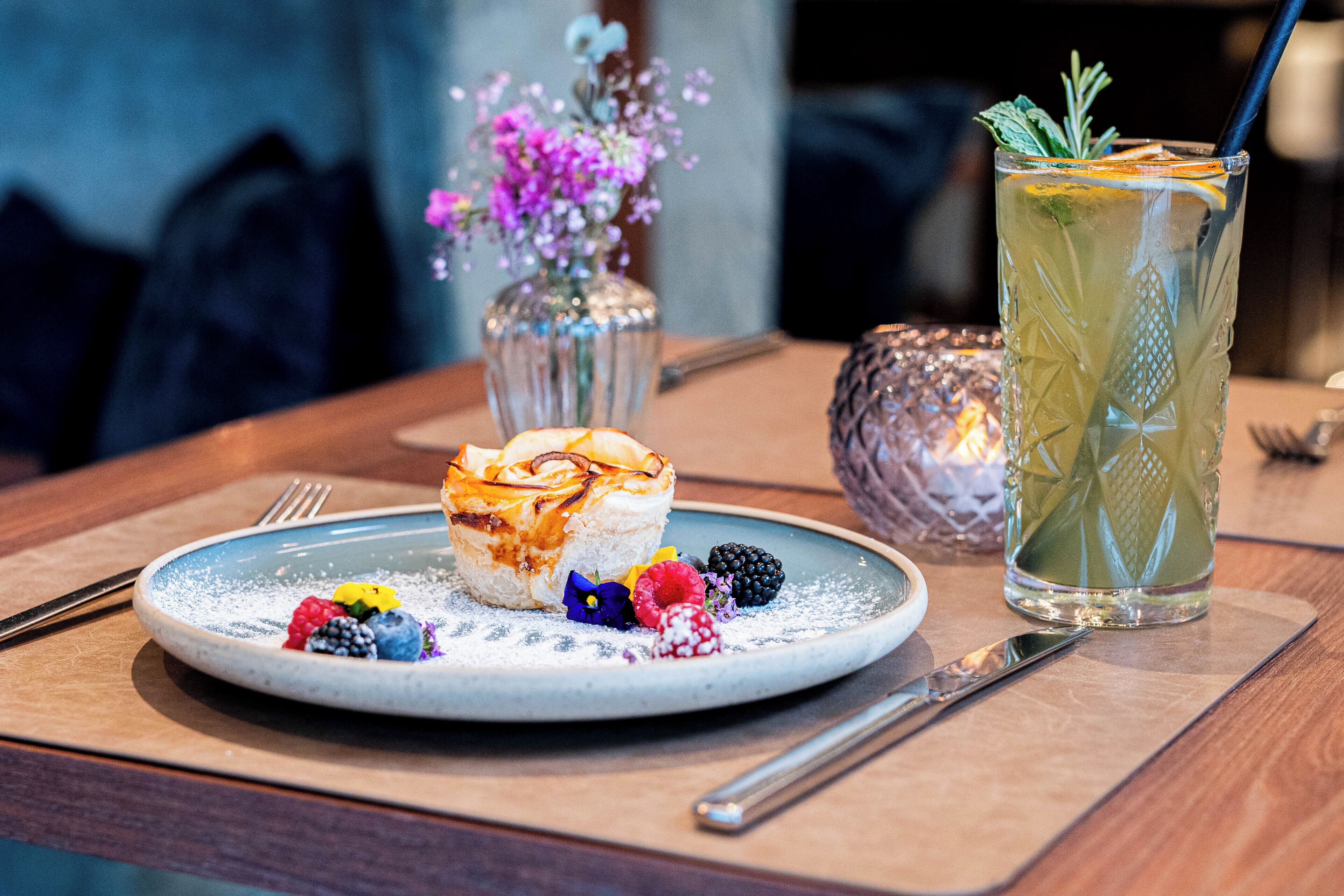 A dessert plate with a pastry, berries, and powdered sugar on a blue plate.