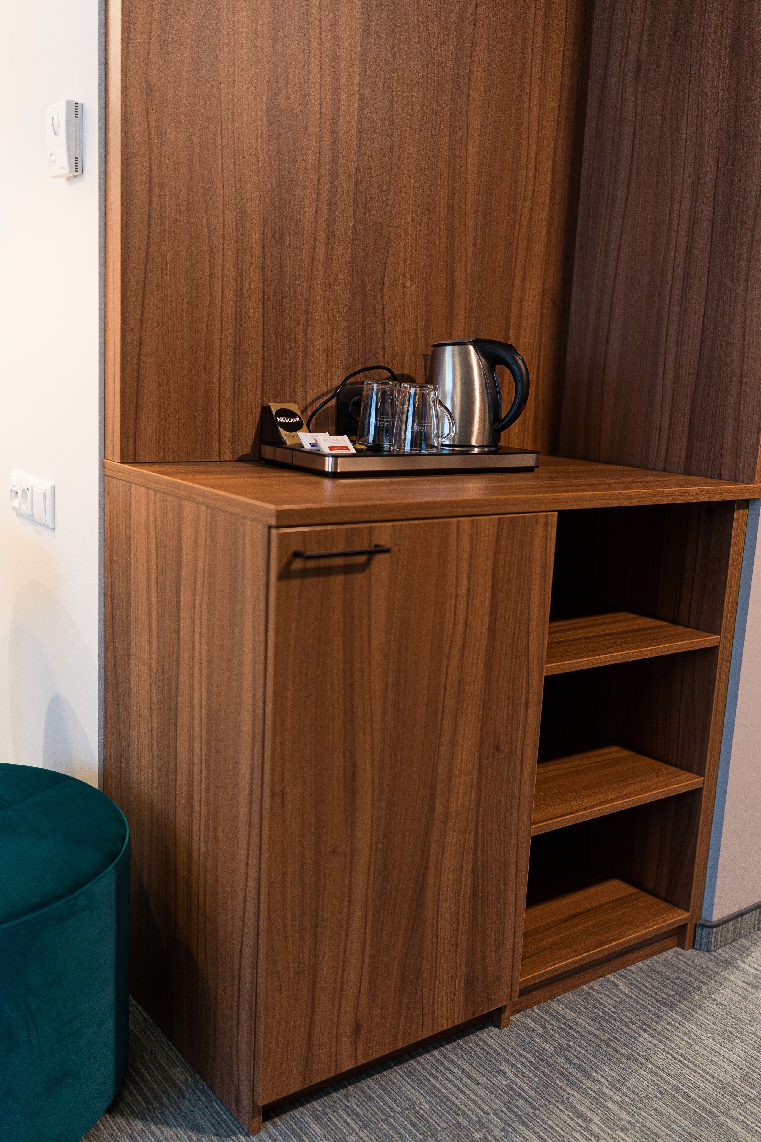 A wooden cabinet with a kettle, a coffee maker, and a tray of glasses.
