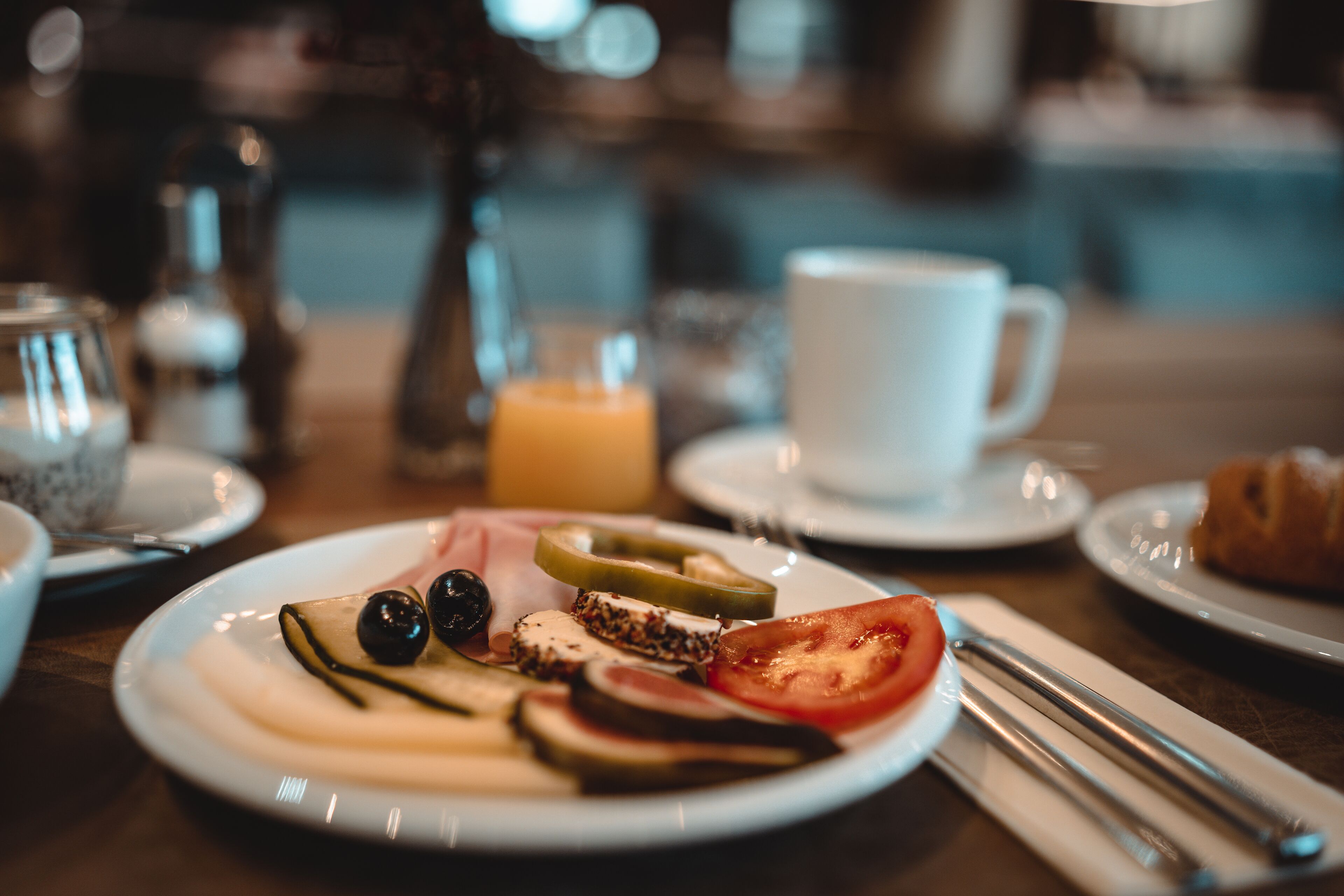 A breakfast plate with various foods, a cup, and a croissant on a table.