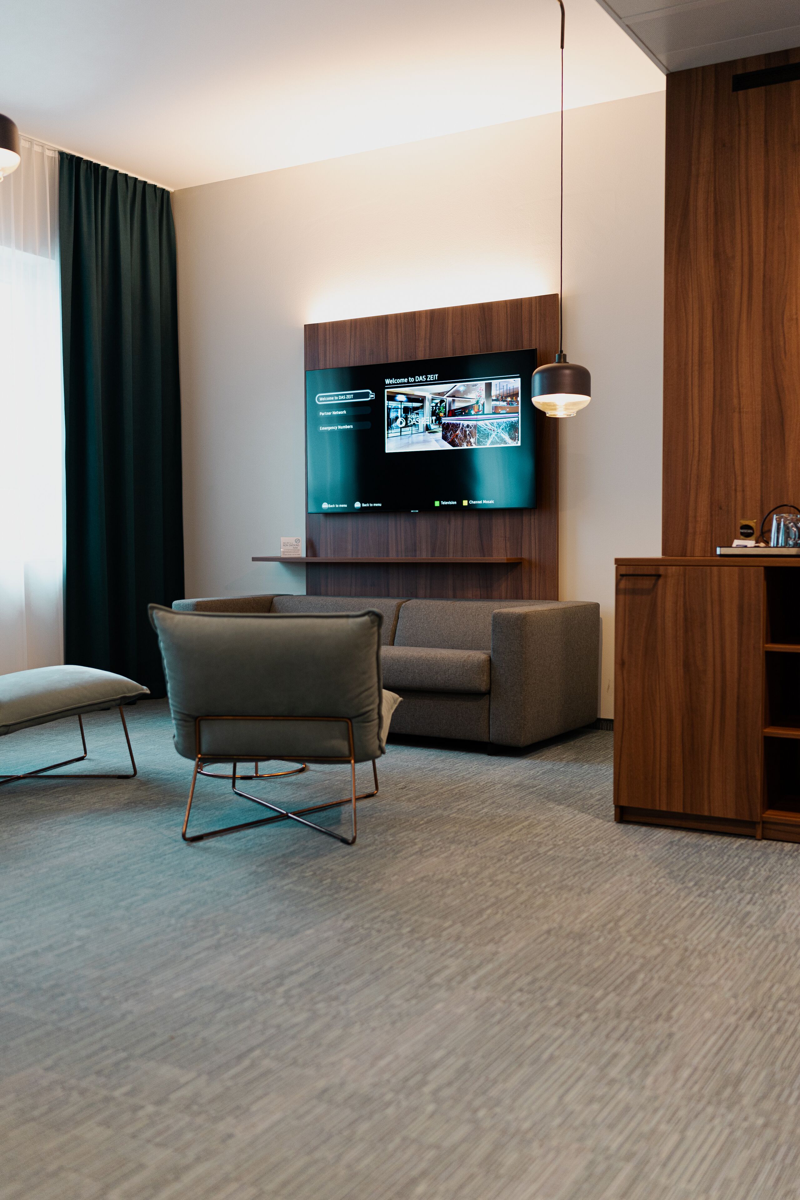 Un salon moderne avec un téléviseur à écran plat fixé au mur, un canapé, un fauteuil et un meuble en bois.