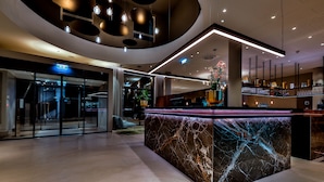 Eine moderne Hotelhalle mit einem Marmor-Rezeptionsschalter, Glastüren und einer Treppe.