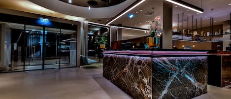 Un moderno vestíbulo de hotel con un mostrador de recepción de mármol, puertas de cristal y una escalera.