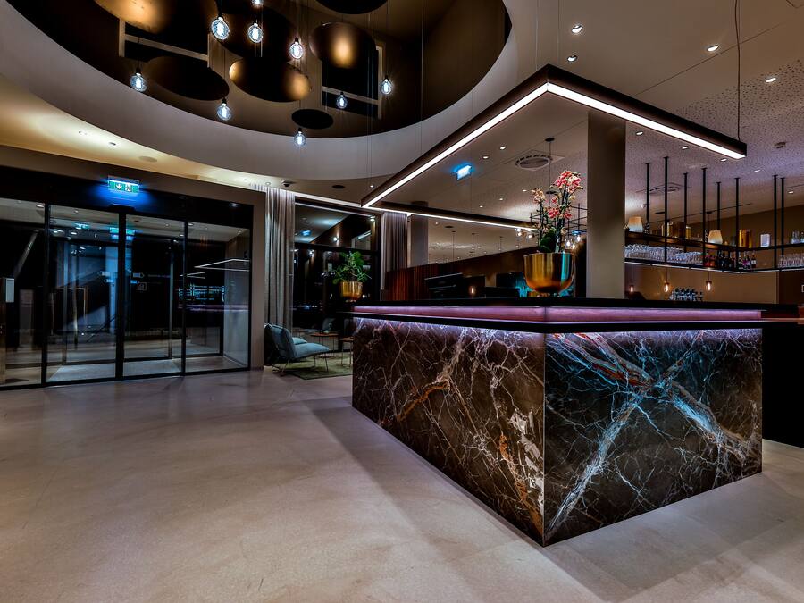 En modern hotellobby med en marmordiskin reception, glasdörrar och en trappa.