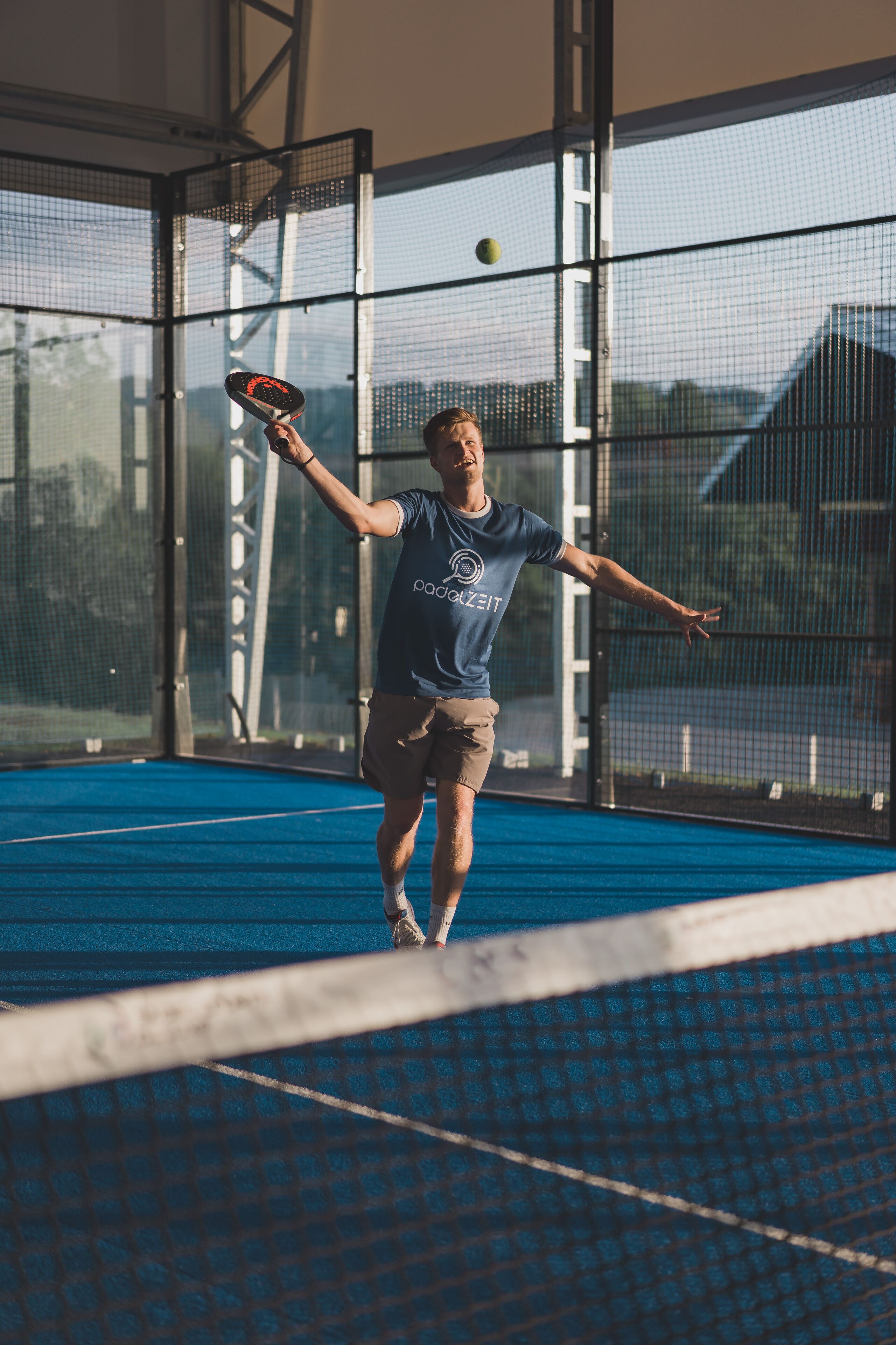A tennis player in a blue shirt and shorts practicing on a blue court with a net.
