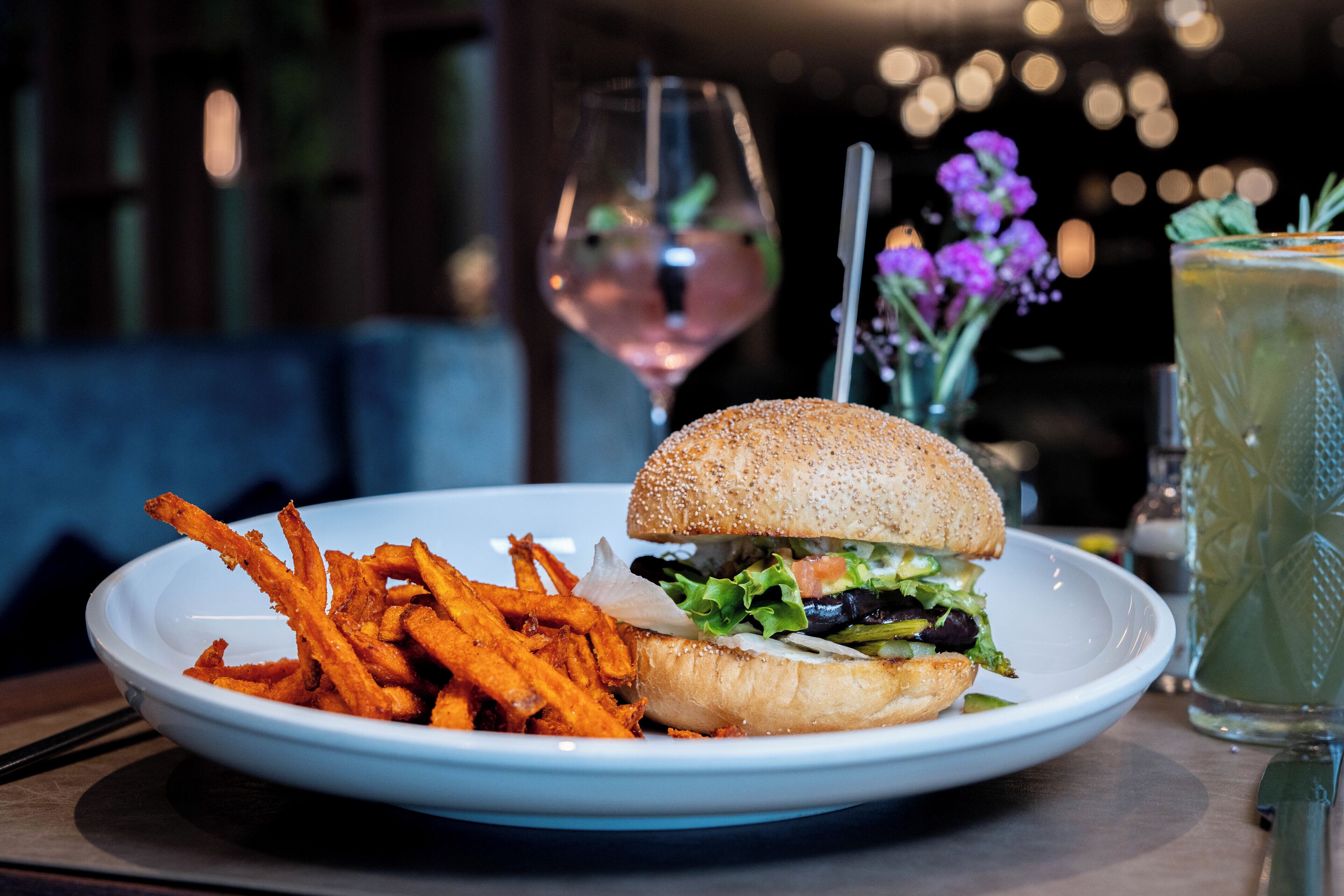 A plate with a burger and fries, a glass of wine, and a drink on a table.