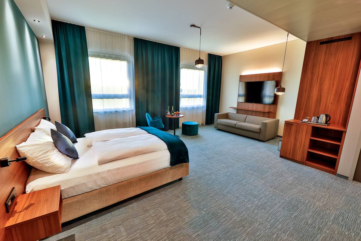 A modern hotel room with a large bed, a sofa, a TV, and a desk.