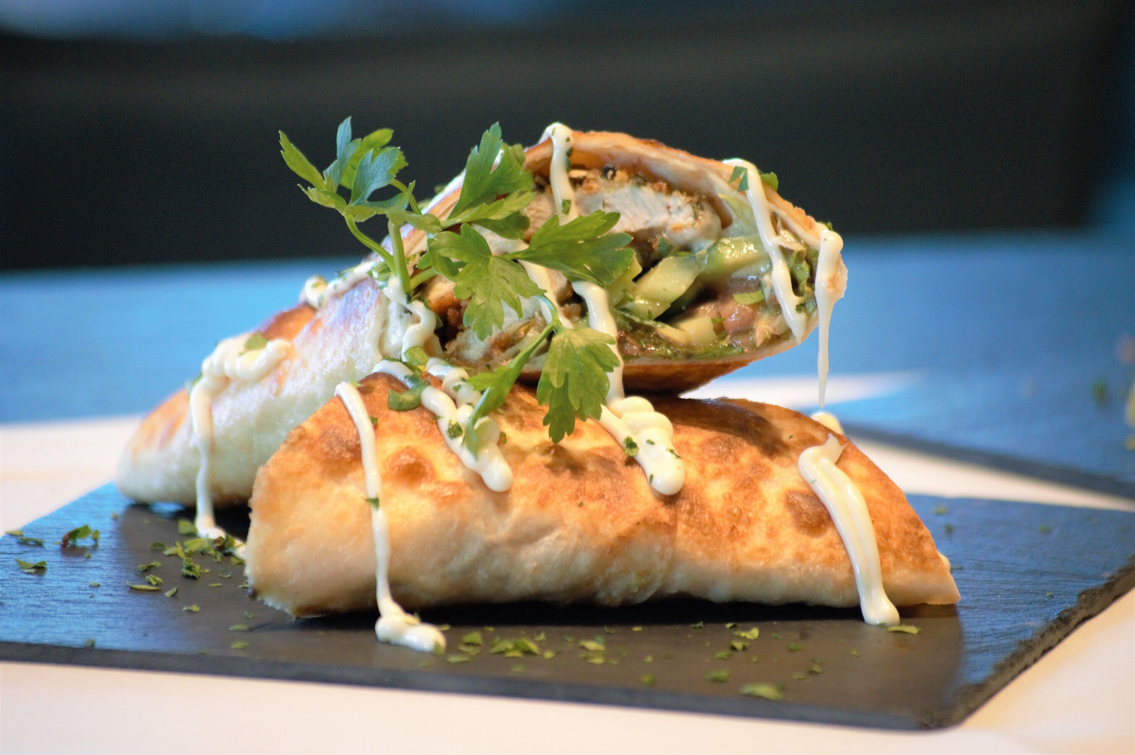 A sandwich on a slate plate with a drizzle of sauce and garnish.