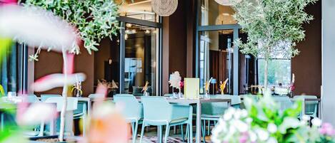 A restaurant with outdoor seating, wicker hanging lights, and potted plants.