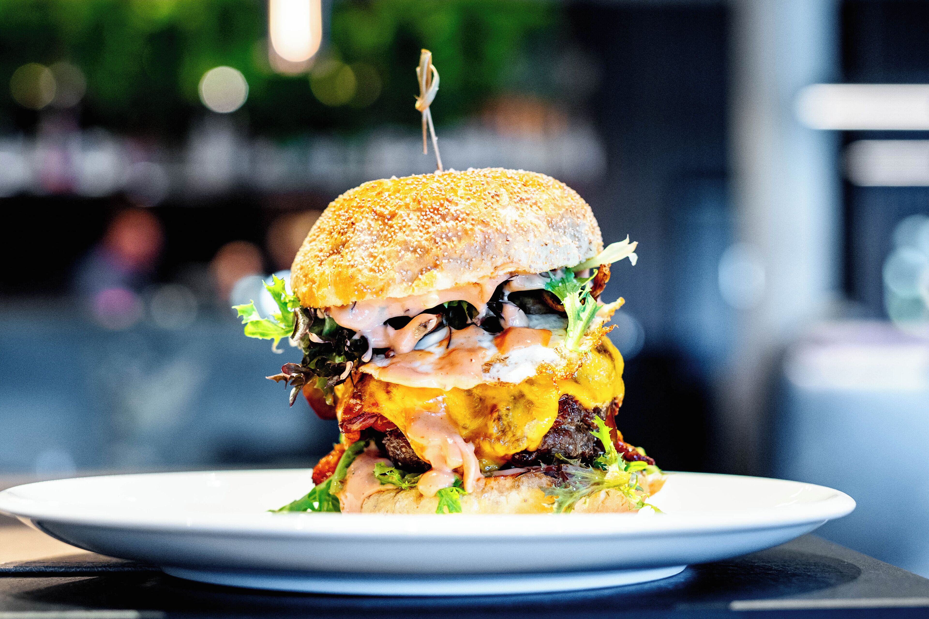 Una hamburguesa grande con pan de sésamo, lechuga, queso y un palillo sobre un plato blanco.