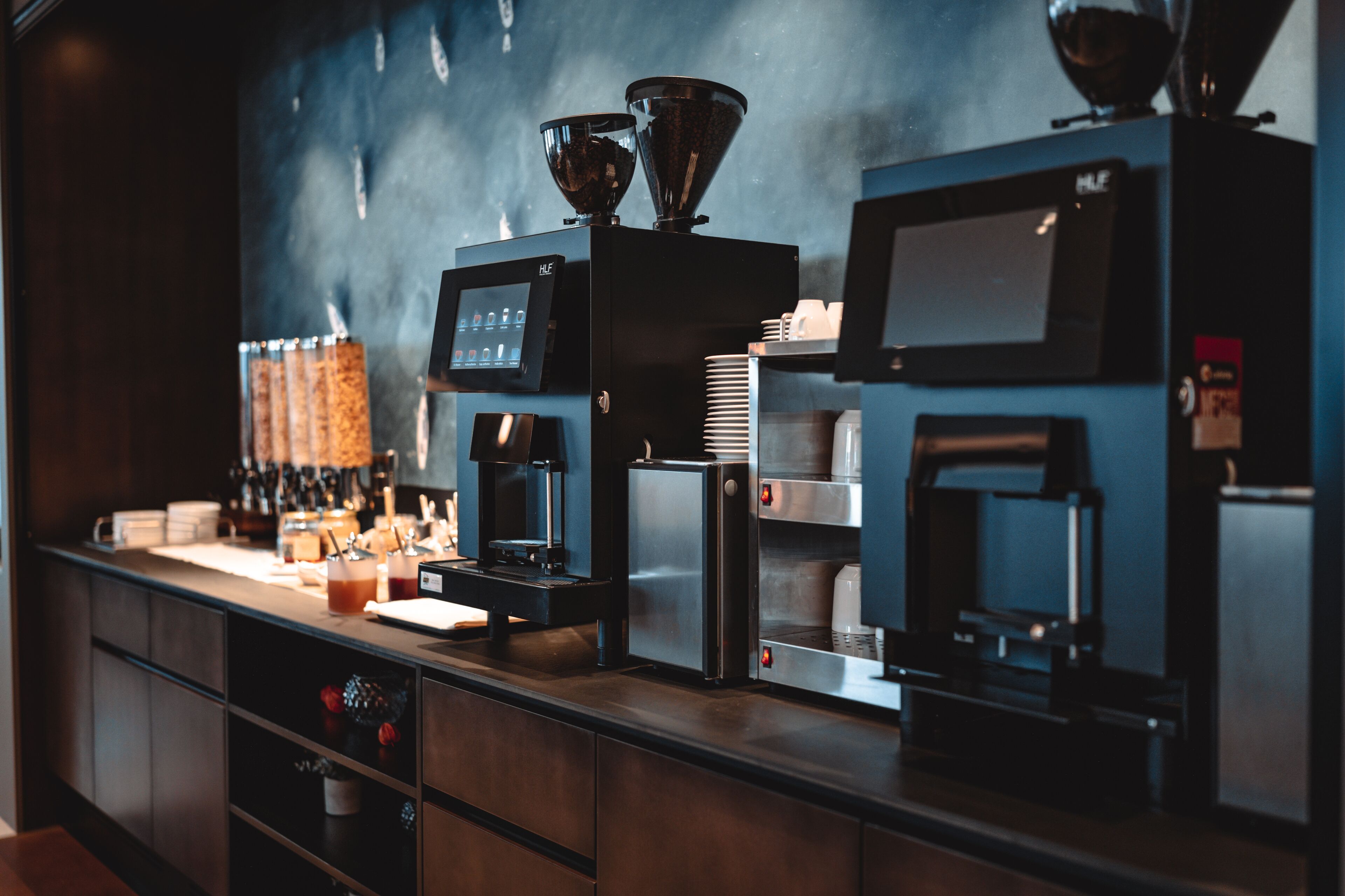 Et professionelt køkken med kaffemaskiner, en vanddispenser og en stempelkande.