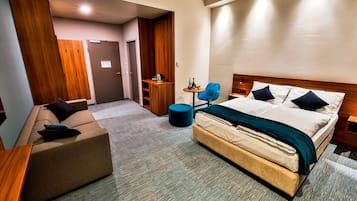 Una habitación de hotel con cama, sofá, una mesita y un armario de madera.