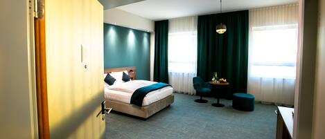 A hotel room with a bed, a desk, a chair, and a small table.