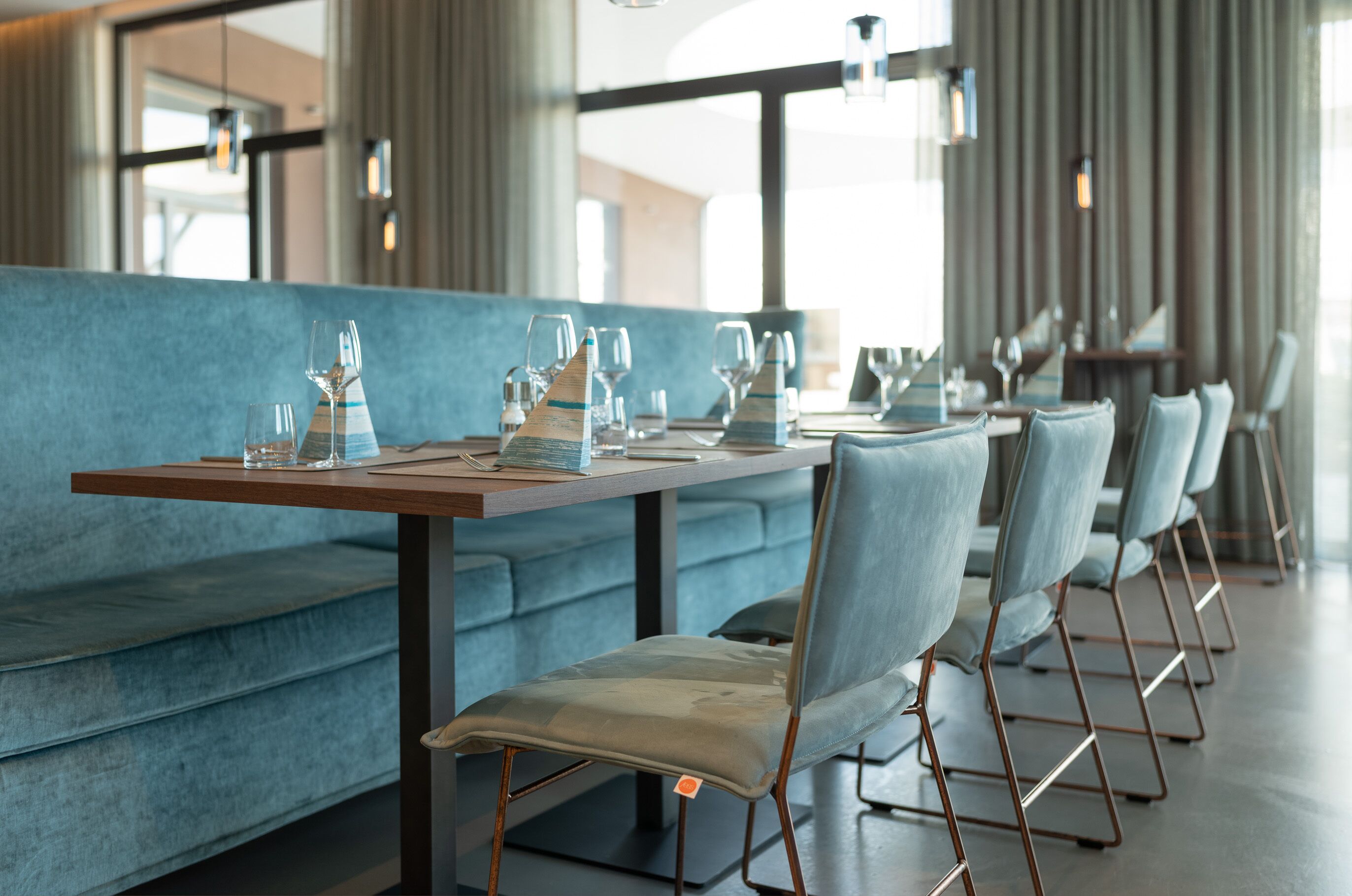 Un restaurante moderno con una larga mesa dispuesta para comer, asientos tapizados en azul y sillas de metal.