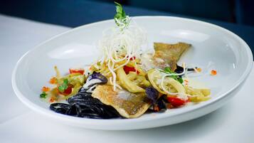 Un plato blanco con una variedad de alimentos, incluyendo fideos, verduras y un trozo de pescado, decorado con hierbas.