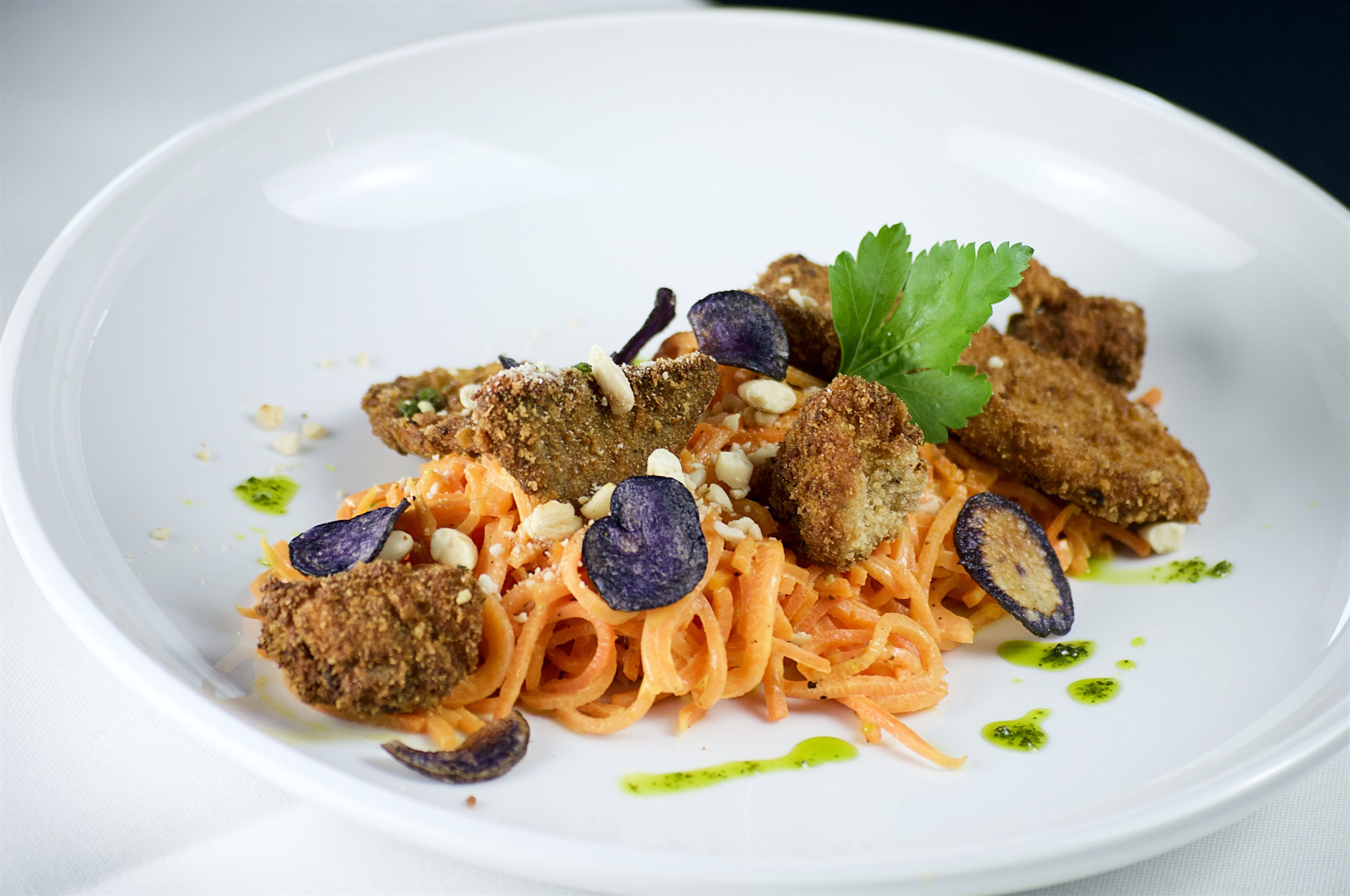 A white plate with pasta, breaded items, and garnishes.