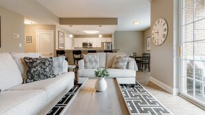 A modern living room with a sofa, coffee table, and a dining area in the background. - Overlook Downtown GVL! (Greenville)