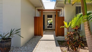 A narrow pathway leading to a wooden door with a glass panel, surrounded by white gravel and potted plants. - Paradise on the Promontory (BANKSIA BEACH)