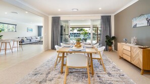 A modern dining area with a wooden table set for six, surrounded by white chairs. - Paradise on the Promontory (BANKSIA BEACH)