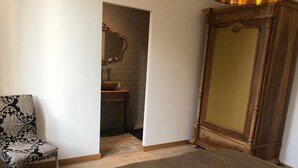 A bedroom with a bed, a chair, a vanity with a mirror, and a wardrobe.