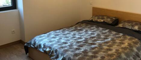 A bedroom with a bed, a chandelier, a window, and an air conditioning unit.