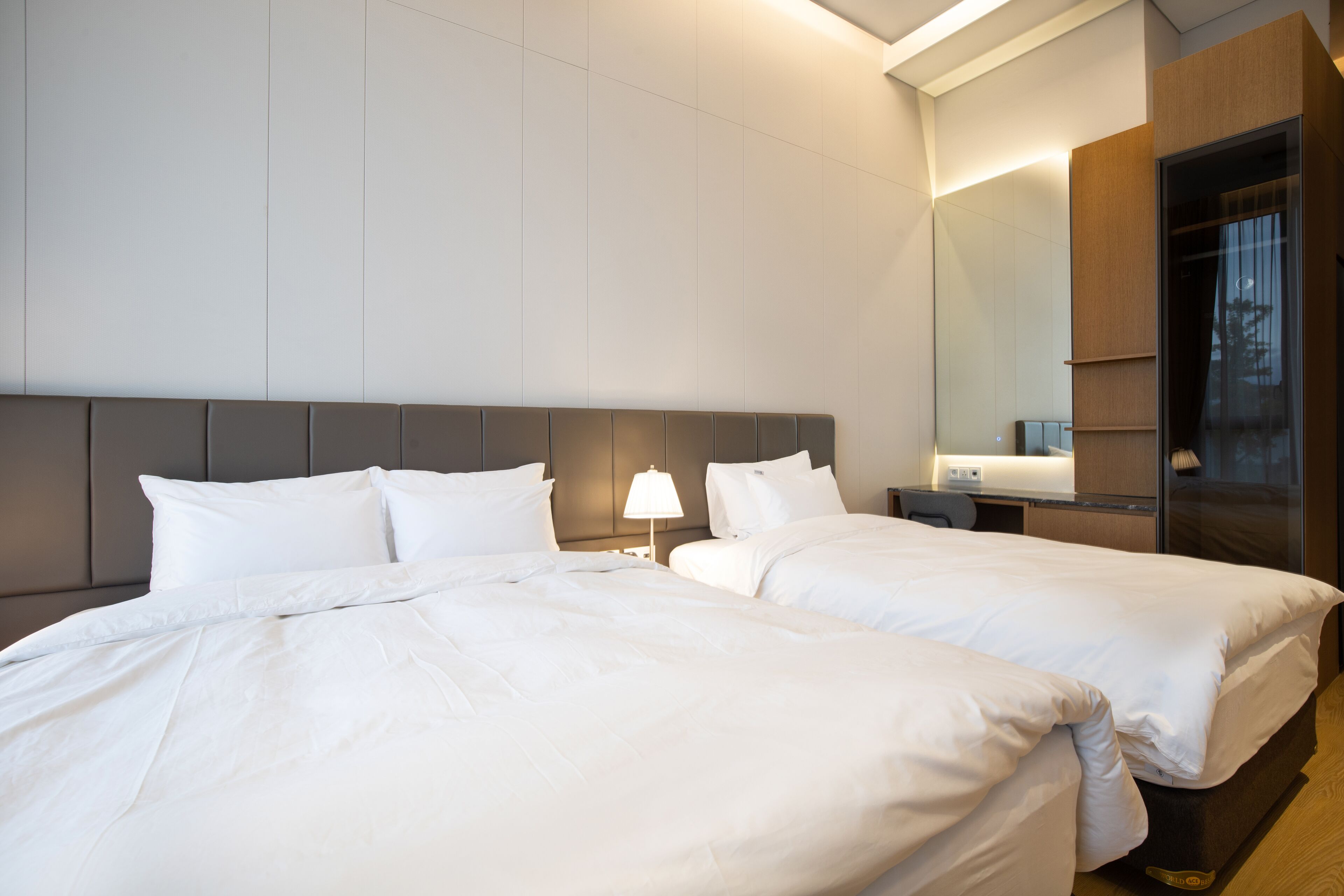 A hotel room with two beds, a nightstand, a lamp, and a large mirror.