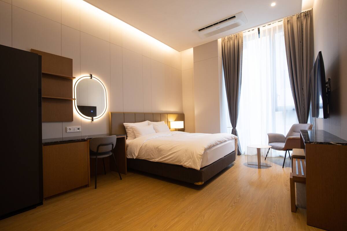 Una habitación de hotel moderna con una cama grande, mesita de noche, silla, escritorio y televisor.