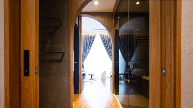 Een hal met houten vloer die leidt naar een kamer met een groot raam, een bank en een stoel.