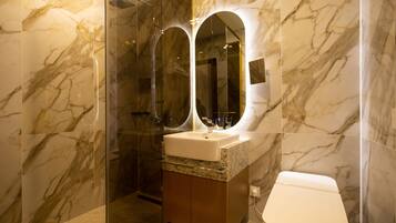 A bathroom with marble walls, a glass shower enclosure, a sink with a mirror, and a toilet.