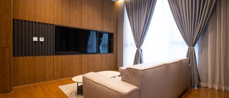 Una sala de estar moderna con piso de madera, un sofá color beige, una mesita blanca pequeña y un televisor de pantalla plana montado en la pared.