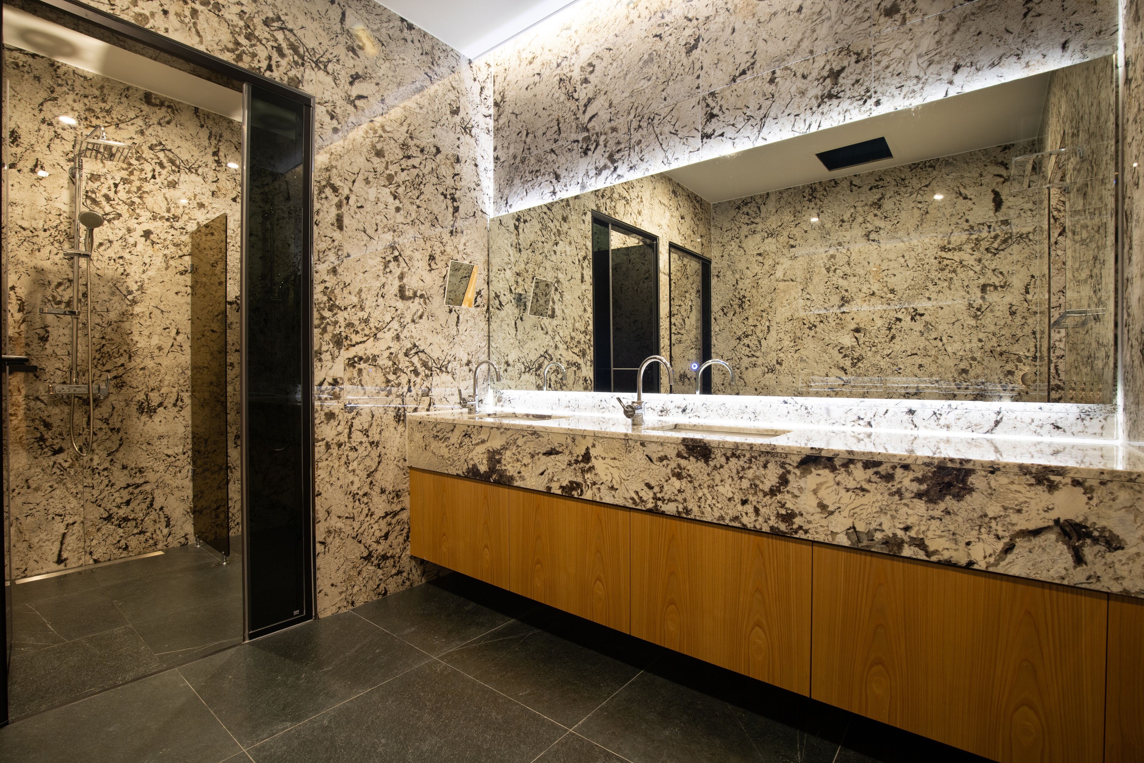Un baño moderno con encimera de granito, muebles de madera y un espejo grande.