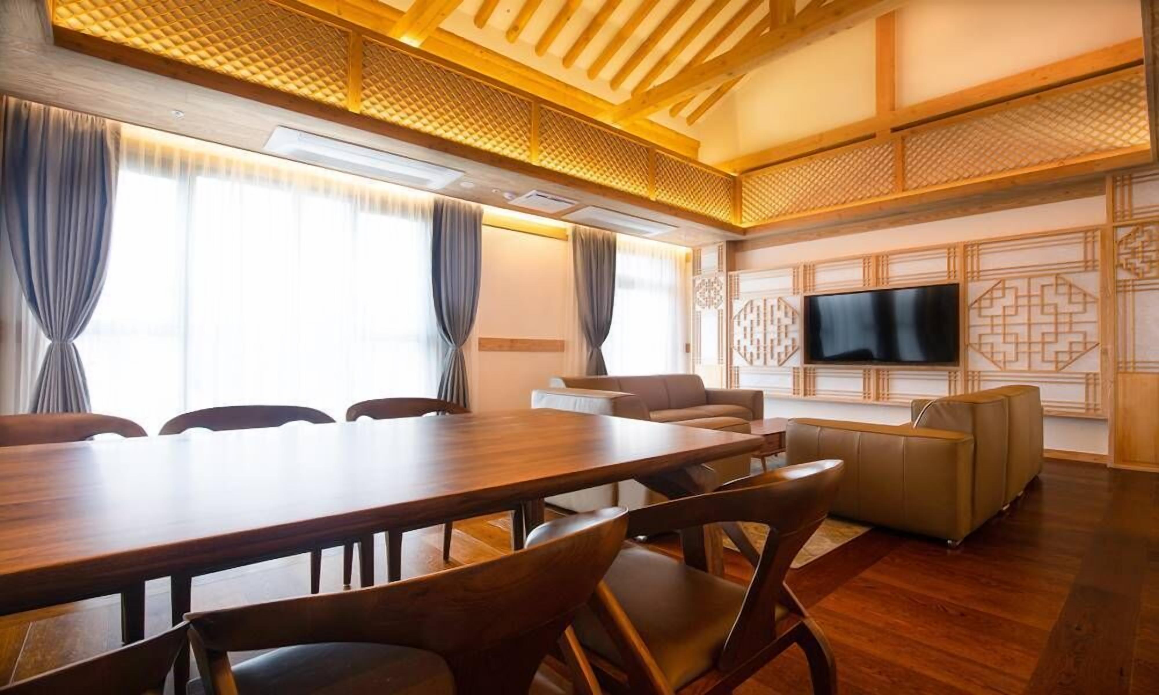 Uma sala de conferências com uma mesa de madeira, cadeiras, um sofá e uma televisão na parede.