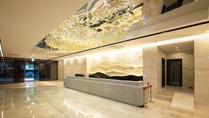 Een moderne lobby met een spiegelende vloer, een receptiebalie en een decoratieve wand met een berglandschap.